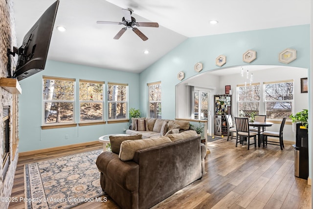 living room featuring ceiling fan, lofted ceiling, a stone fireplace, and hardwood / wood-style floors