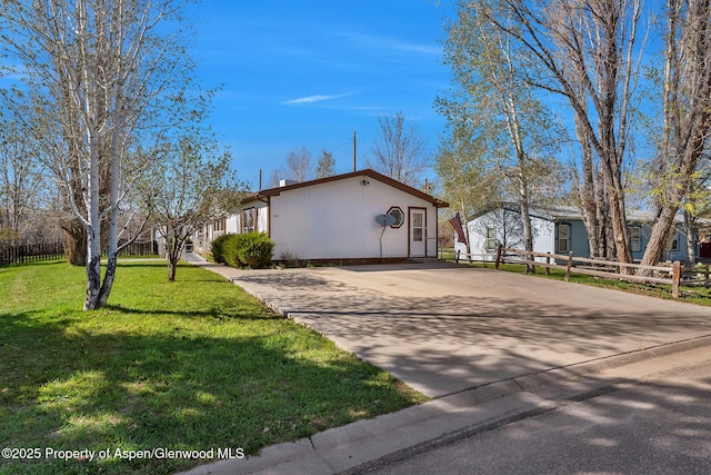 view of side of property featuring fence, concrete driveway, and a lawn