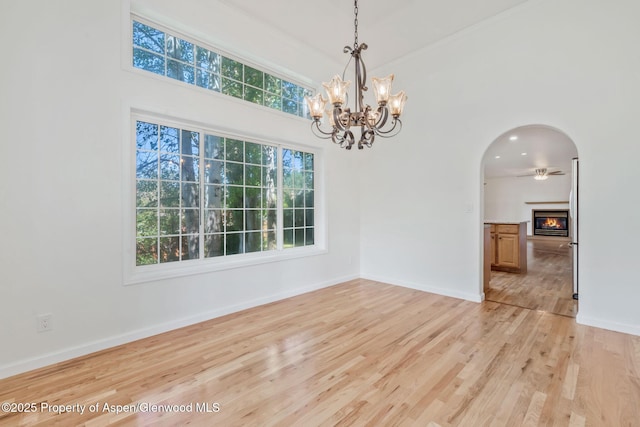 1020 Alta Vista Dr, Craig, CO 81625 - spare room with arched walkways, light wood-type flooring, a chandelier, a warm lit fireplace, and a towering ceiling