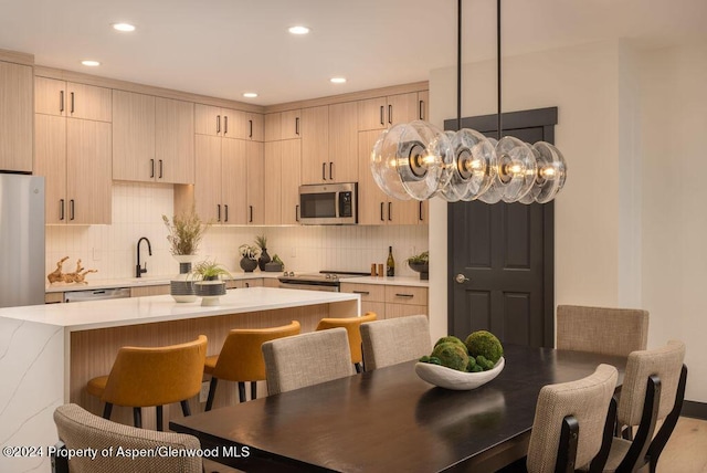 kitchen with light countertops, a breakfast bar area, decorative backsplash, stainless steel appliances, and light brown cabinetry