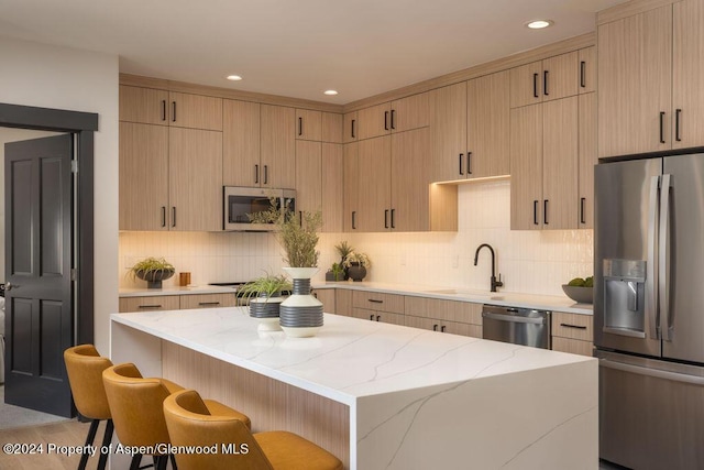 kitchen with tasteful backsplash, a breakfast bar, a center island, appliances with stainless steel finishes, and a sink
