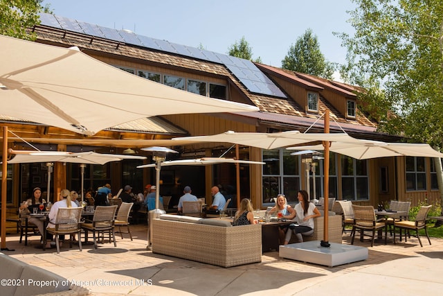 back of house featuring outdoor dining space, a patio, roof mounted solar panels, and an outdoor hangout area