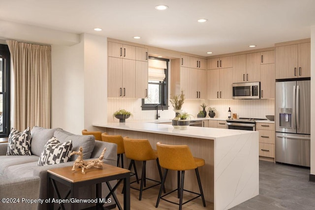 kitchen with stainless steel appliances, a peninsula, a breakfast bar area, and light brown cabinetry