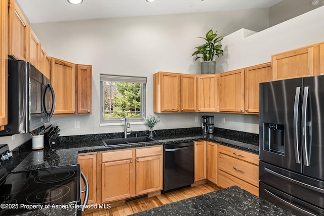 kitchen with light wood finished floors, a sink, black appliances, and dark stone countertops