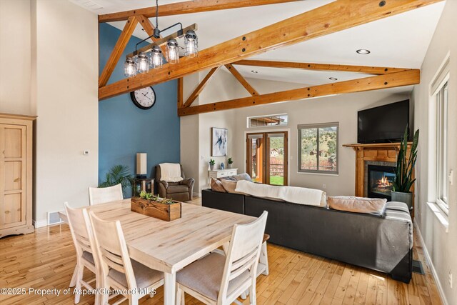 dining room featuring a glass covered fireplace, light wood finished floors, baseboards, and beam ceiling