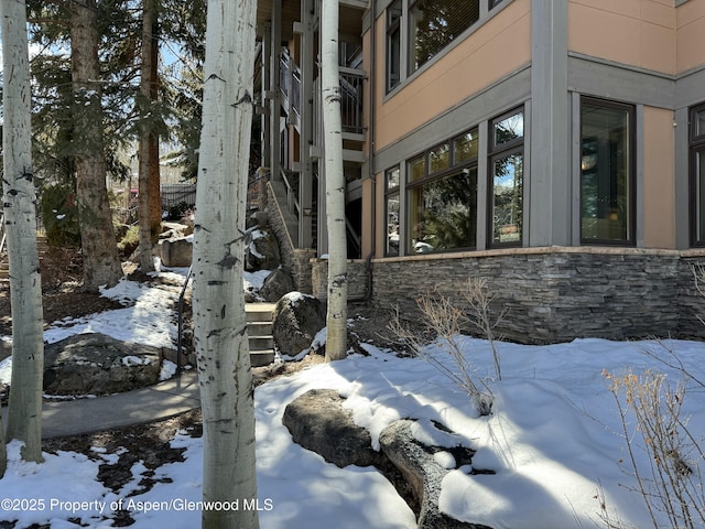 snow covered property featuring stone siding