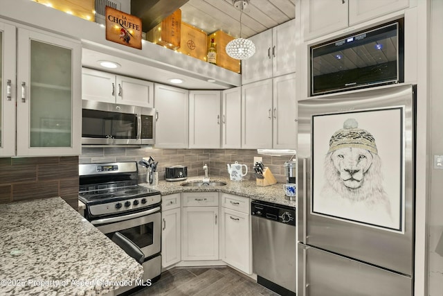 kitchen with tasteful backsplash, white cabinets, appliances with stainless steel finishes, light stone countertops, and a sink