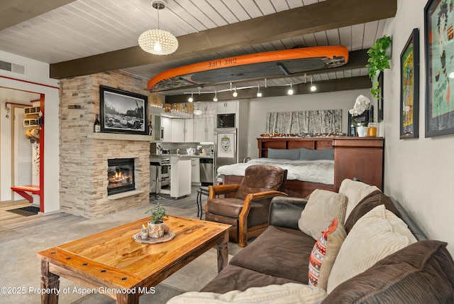 living area with a stone fireplace, beamed ceiling, wooden ceiling, and visible vents