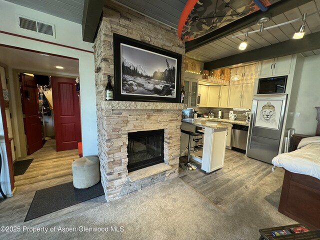 kitchen featuring stainless steel dishwasher, beamed ceiling, a fireplace, and visible vents