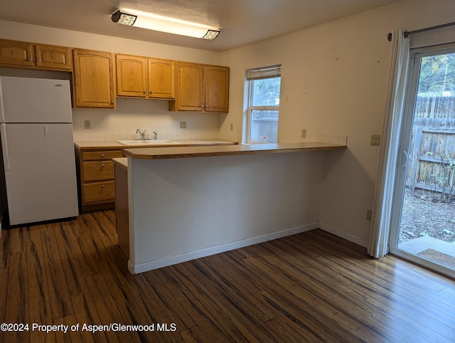 kitchen with kitchen peninsula, sink, dark hardwood / wood-style floors, and white refrigerator