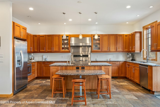 kitchen with appliances with stainless steel finishes, light stone counters, a kitchen island with sink, a sink, and exhaust hood