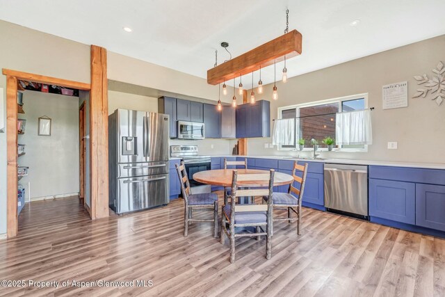 kitchen with light wood finished floors, stainless steel appliances, light countertops, and decorative light fixtures