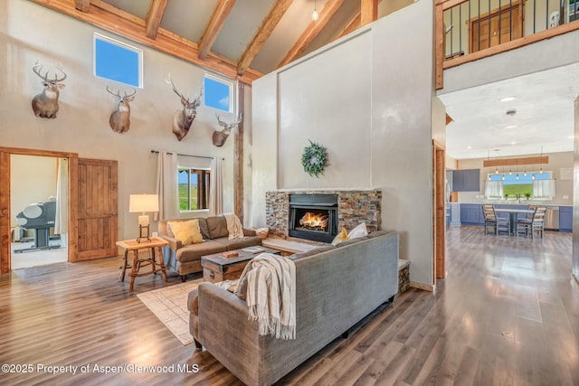 living area with high vaulted ceiling, a stone fireplace, wood finished floors, and beam ceiling