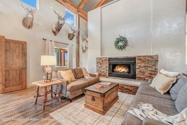 living area with a stone fireplace, light wood-style flooring, and a towering ceiling