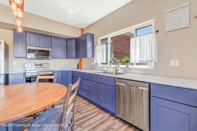 kitchen with a sink, light wood-style floors, light countertops, appliances with stainless steel finishes, and blue cabinetry