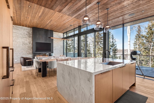 kitchen featuring expansive windows, light stone counters, wood ceiling, and a sink