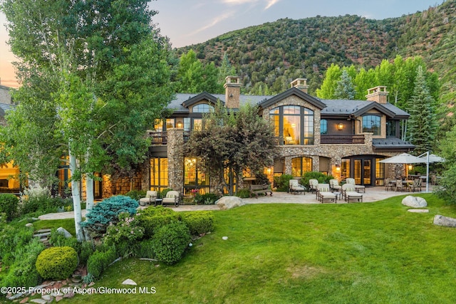 120 Running Mare Rd, Woody Creek, CO 81656 - back of property at dusk with stone siding, a patio, a mountain view, a balcony, and a lawn