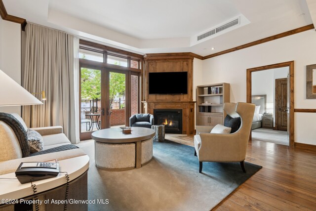 living room featuring a fireplace, hardwood / wood-style flooring, a tray ceiling, and crown molding