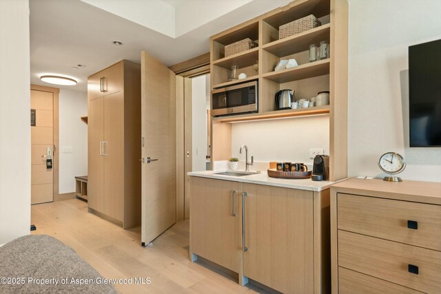 kitchen with stainless steel microwave, light brown cabinetry, sink, and light hardwood / wood-style floors