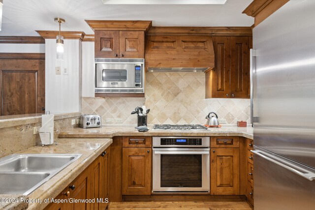 kitchen featuring sink, stainless steel appliances, wall chimney range hood, pendant lighting, and decorative backsplash