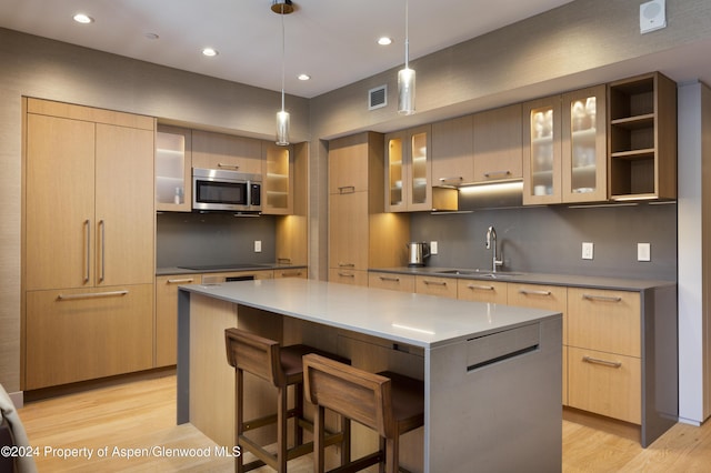 kitchen featuring a breakfast bar, light brown cabinets, sink, light hardwood / wood-style floors, and a kitchen island