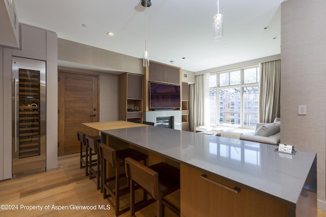 kitchen featuring hanging light fixtures, light hardwood / wood-style floors, beverage cooler, and a breakfast bar area