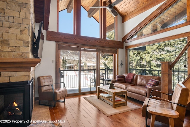 living area with wood ceiling, beam ceiling, hardwood / wood-style floors, and a stone fireplace