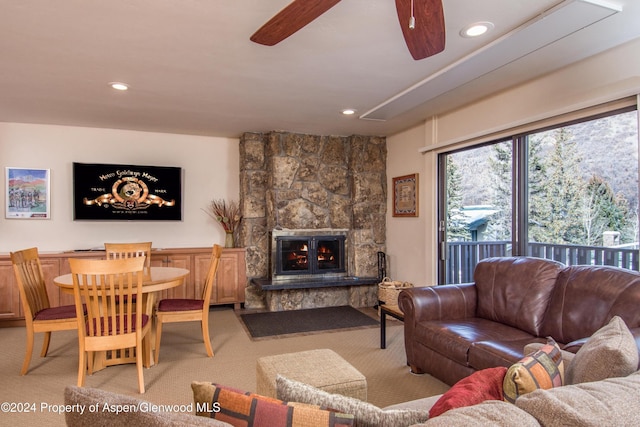 living room featuring ceiling fan, a stone fireplace, and light carpet