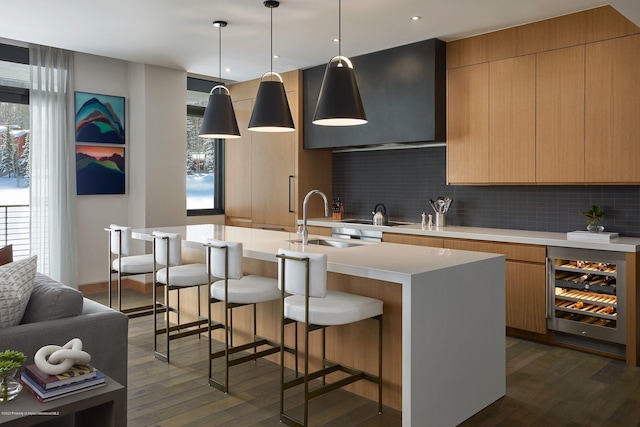 kitchen with sink, beverage cooler, backsplash, an island with sink, and decorative light fixtures