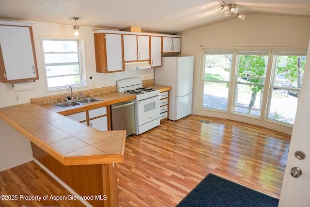 kitchen with sink, kitchen peninsula, lofted ceiling, white appliances, and white cabinets