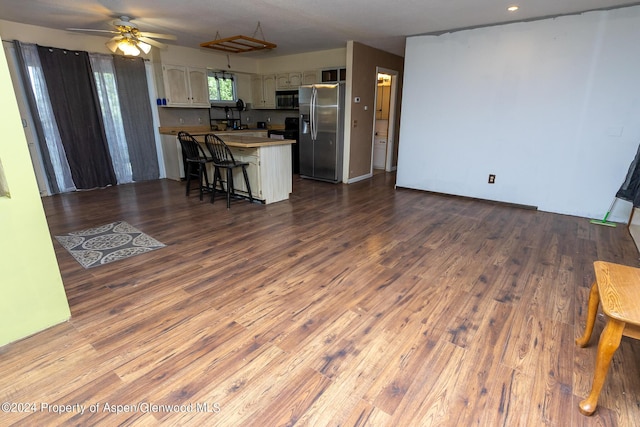 kitchen featuring kitchen peninsula, appliances with stainless steel finishes, a breakfast bar, ceiling fan, and wood-type flooring