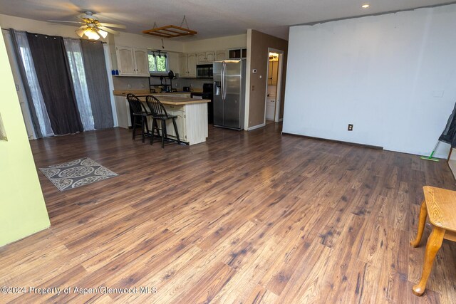 kitchen featuring kitchen peninsula, appliances with stainless steel finishes, a breakfast bar, ceiling fan, and wood-type flooring