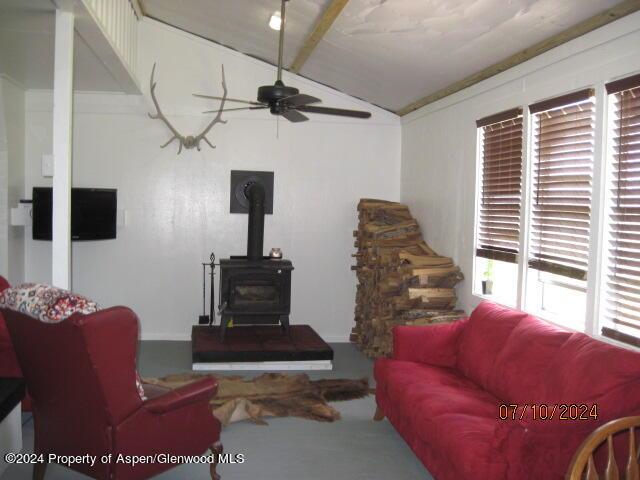 living room with a wood stove, ceiling fan, and lofted ceiling