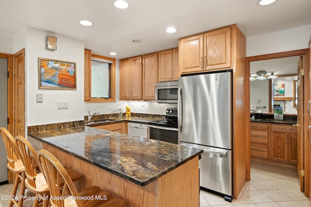 kitchen featuring sink, stainless steel appliances, kitchen peninsula, dark stone countertops, and a breakfast bar area