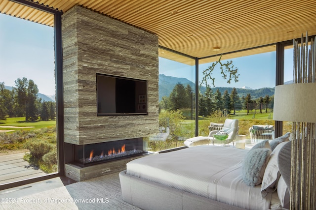 bedroom featuring an outdoor stone fireplace, multiple windows, and wood ceiling