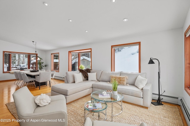 living room with vaulted ceiling, a baseboard heating unit, light wood-type flooring, and a healthy amount of sunlight