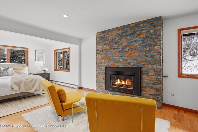 bedroom featuring light hardwood / wood-style floors, a stone fireplace, and a baseboard radiator