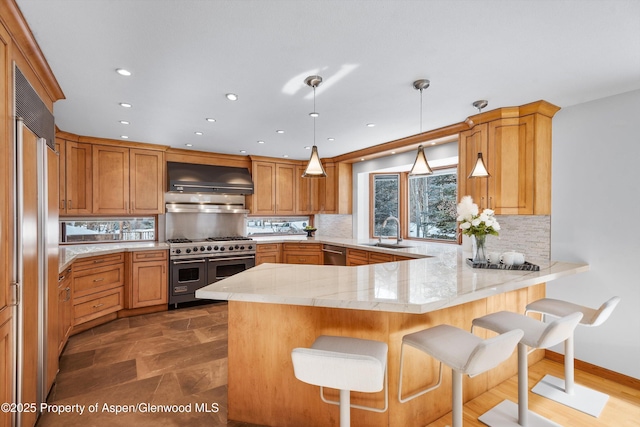 kitchen with wall chimney exhaust hood, decorative light fixtures, a kitchen bar, high end appliances, and kitchen peninsula