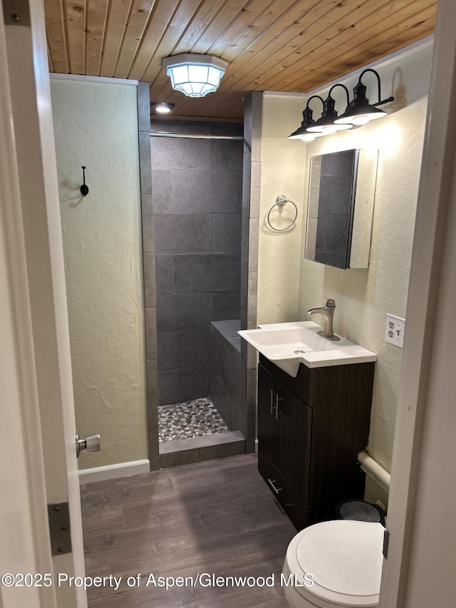 bathroom featuring a tile shower, vanity, wooden ceiling, and toilet