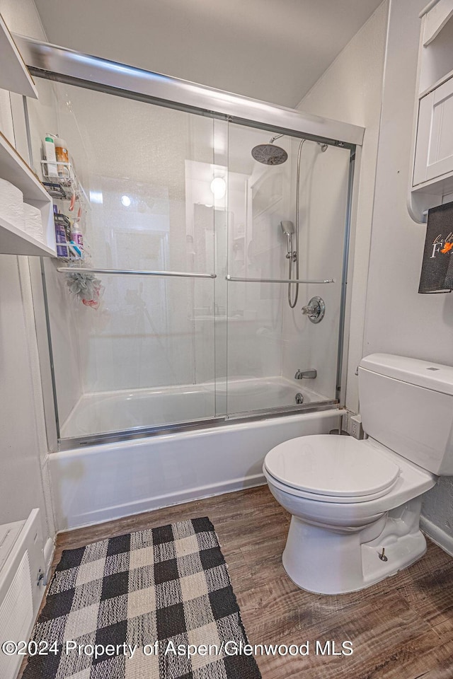 bathroom with combined bath / shower with glass door, hardwood / wood-style floors, and toilet