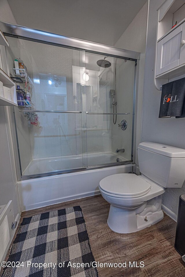 bathroom with hardwood / wood-style flooring, toilet, and shower / bath combination with glass door