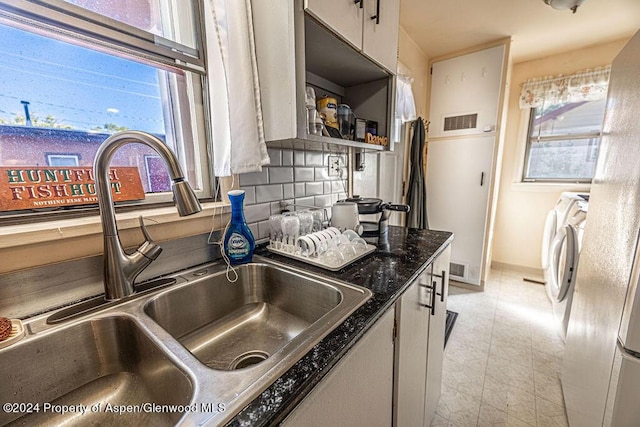 kitchen with backsplash, white cabinets, sink, dark stone countertops, and separate washer and dryer