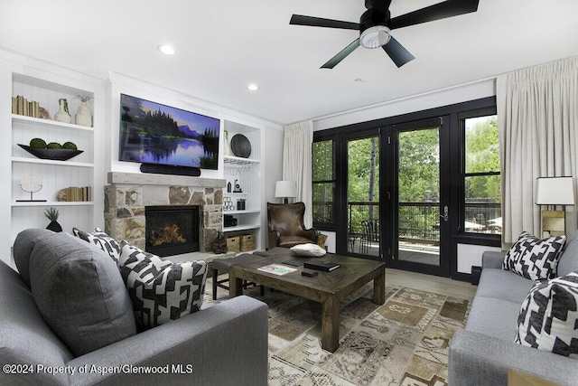 living room with built in shelves, ceiling fan, a fireplace, and light hardwood / wood-style floors