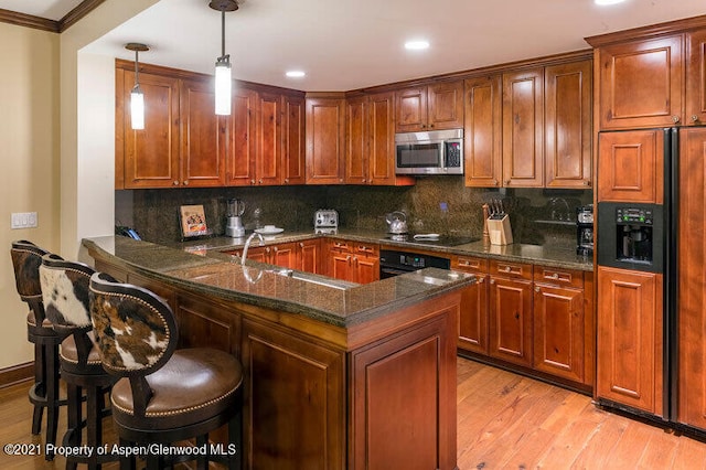 kitchen featuring kitchen peninsula, a kitchen breakfast bar, sink, black appliances, and pendant lighting