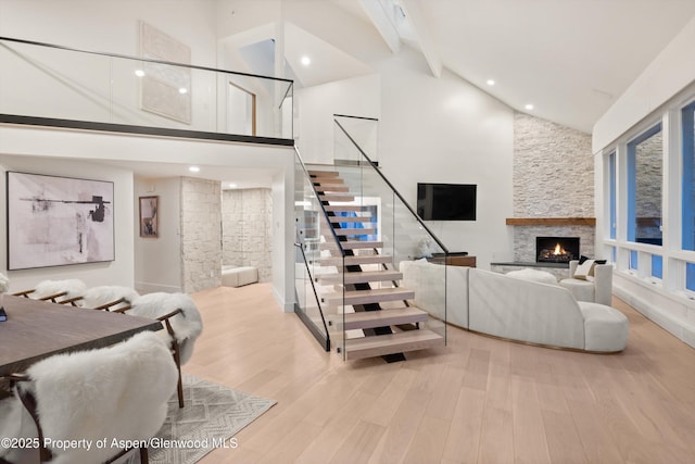 staircase featuring beam ceiling, a stone fireplace, hardwood / wood-style floors, and high vaulted ceiling