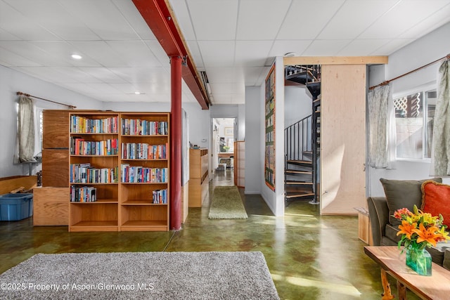 living area featuring stairway, a paneled ceiling, and concrete flooring