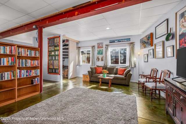 living area featuring a drop ceiling, finished concrete flooring, and baseboards