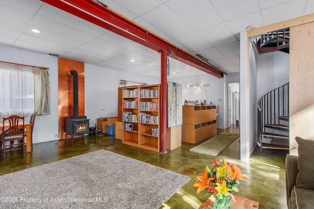 interior space with concrete floors, a drop ceiling, stairs, recessed lighting, and a wood stove