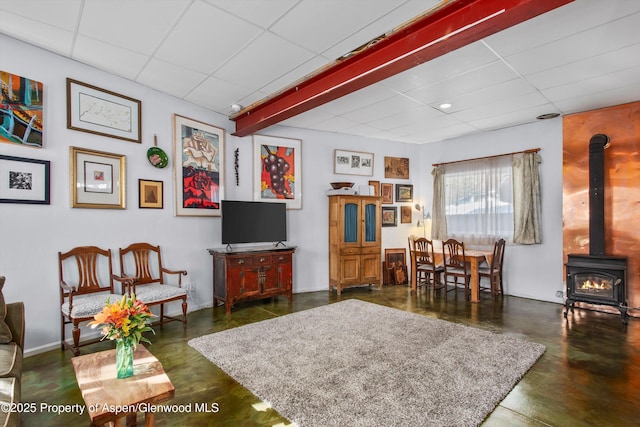 living area with a wood stove, a paneled ceiling, and concrete floors