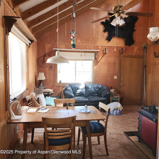 living area with a healthy amount of sunlight, lofted ceiling with beams, carpet flooring, and wood walls